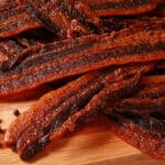 A pile of black pepper bacon jerky on a cutting board.