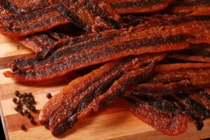 A pile of black pepper bacon jerky on a cutting board.