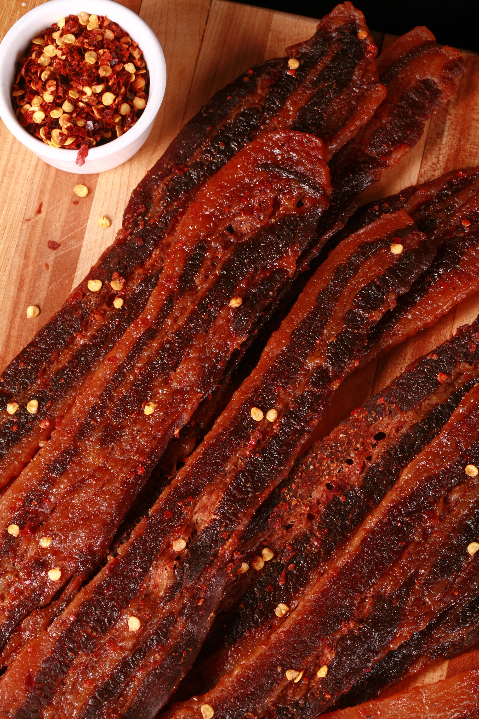 A pile of homemade sweet and spicy bacon jerky on a wooden cutting board.
