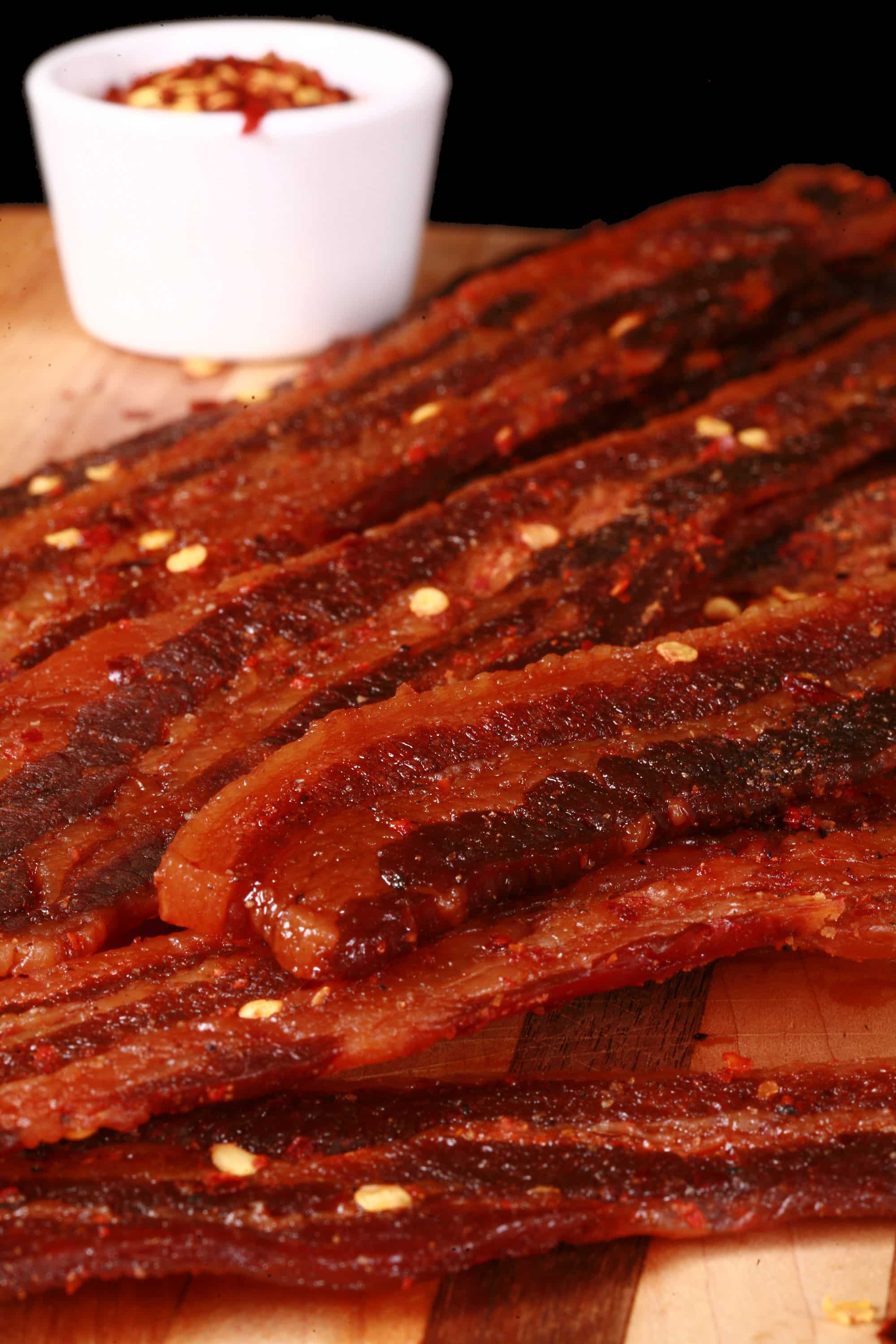 A pile of sweet and spicy homemade bacon jerky on a wooden cutting board.