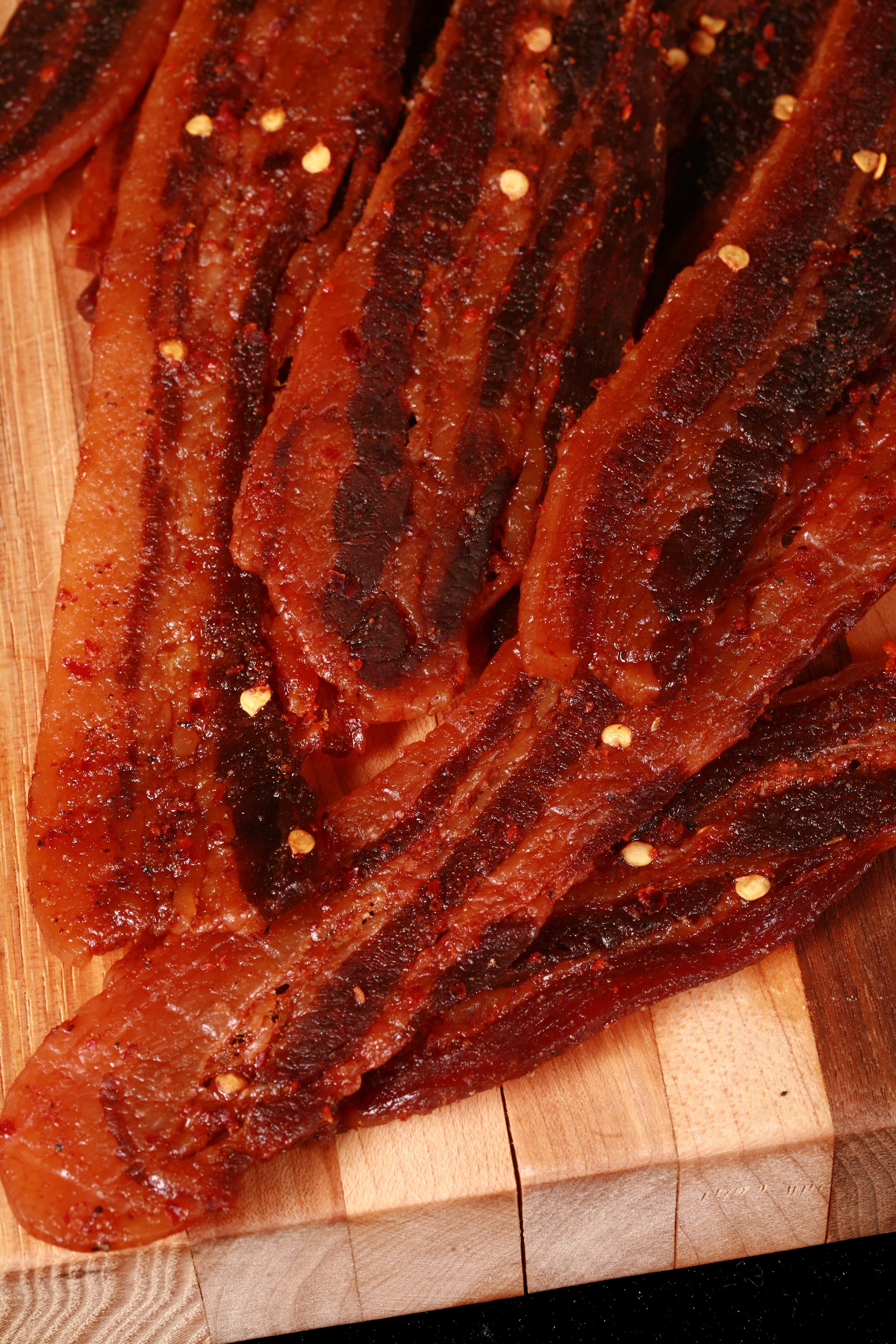 A pile of homemade sweet and spicy bacon jerky on a wooden cutting board.