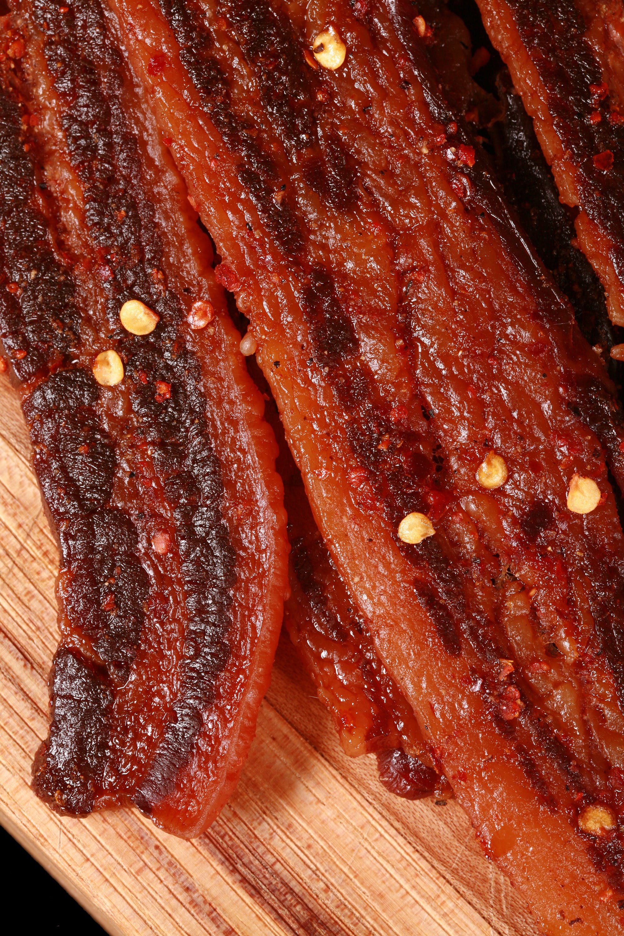 A pile of sweet and spicy homemade bacon jerky on a wooden cutting board.