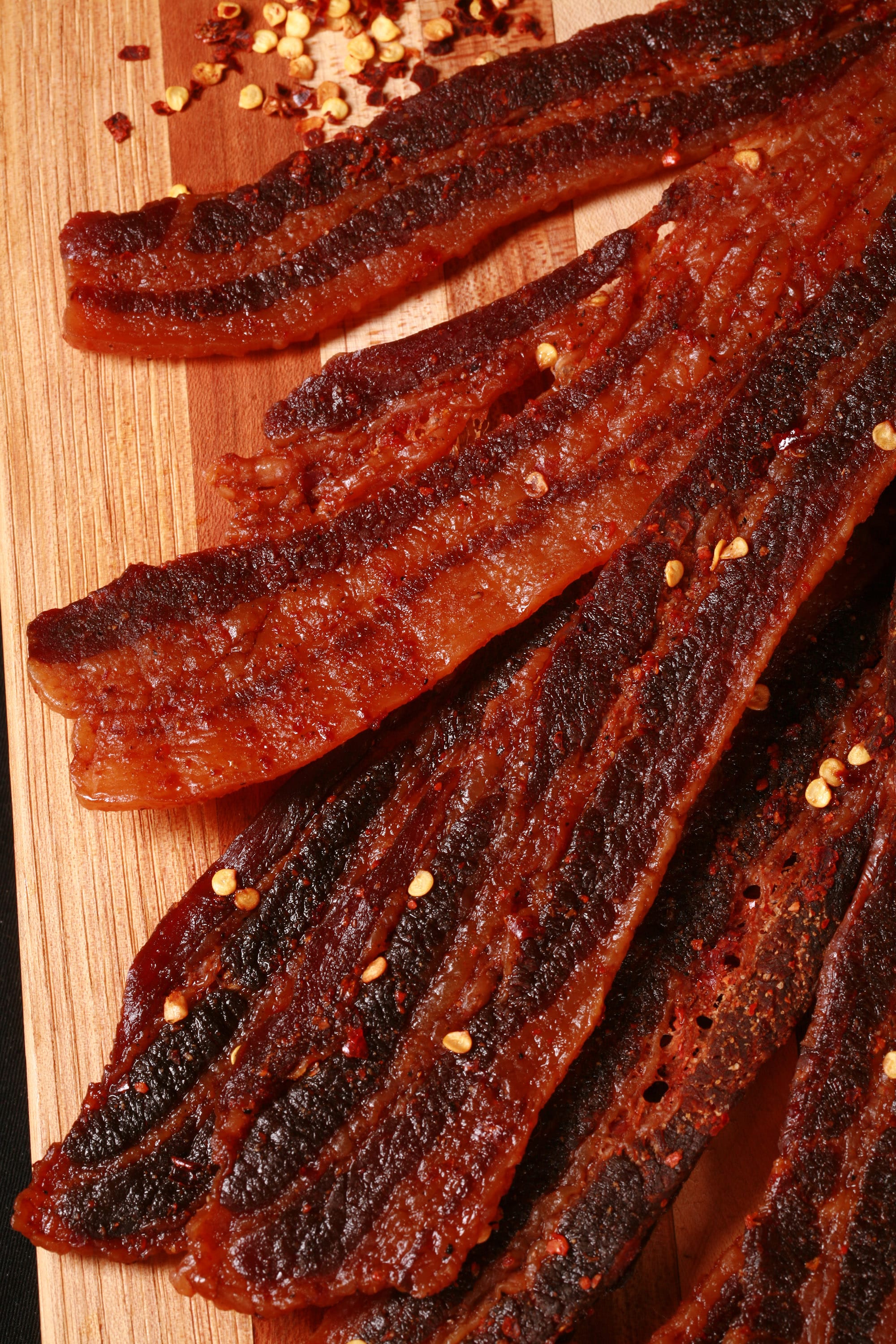 A pile of homemade sweet and spicy bacon jerky on a wooden cutting board.
