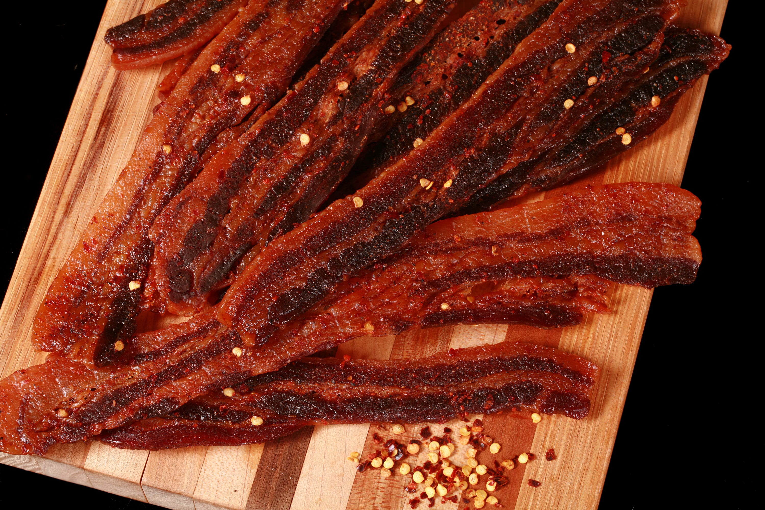 A pile of sweet and spicy homemade bacon jerky on a wooden cutting board.