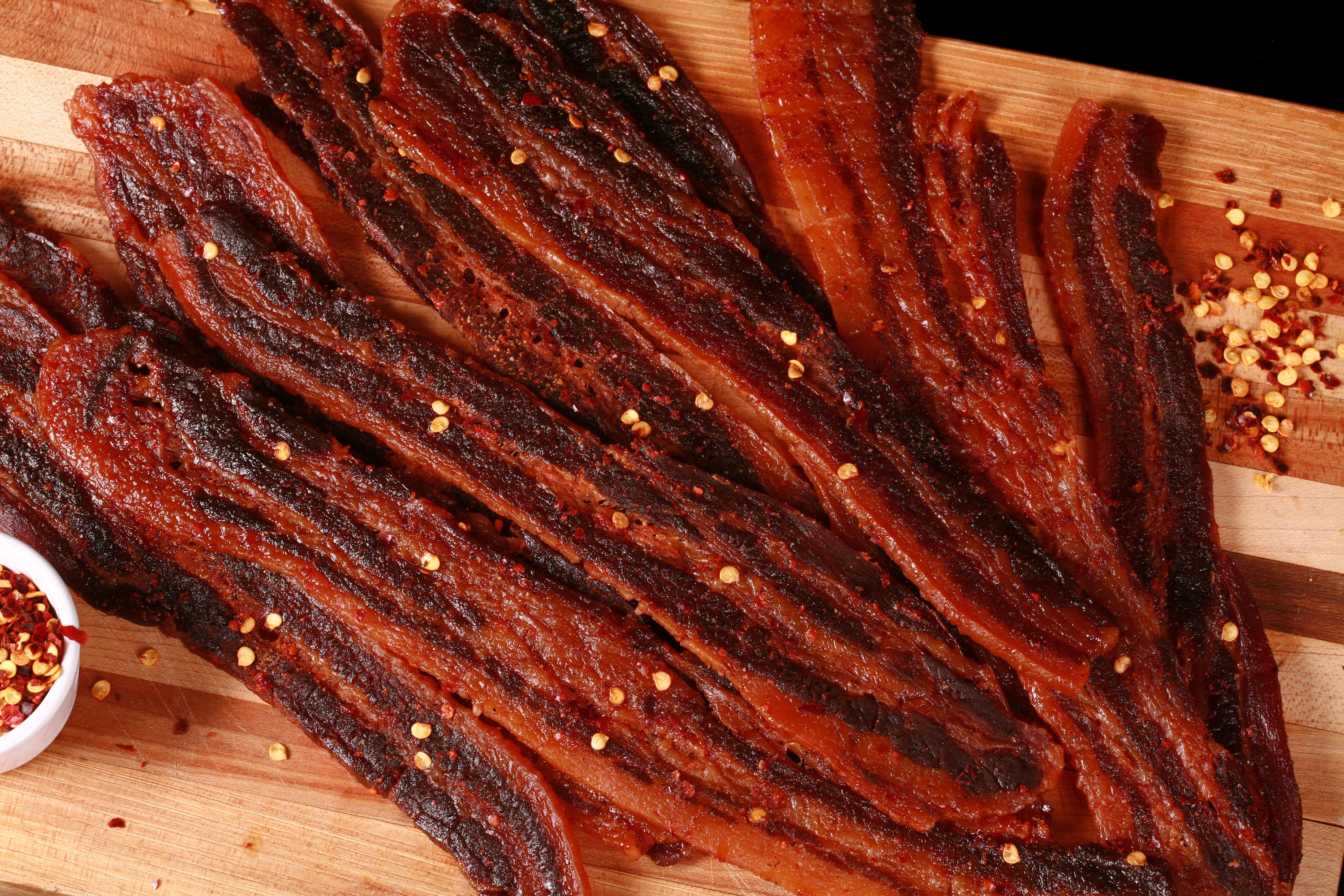 A pile of homemade sweet and spicy bacon jerky on a wooden cutting board.