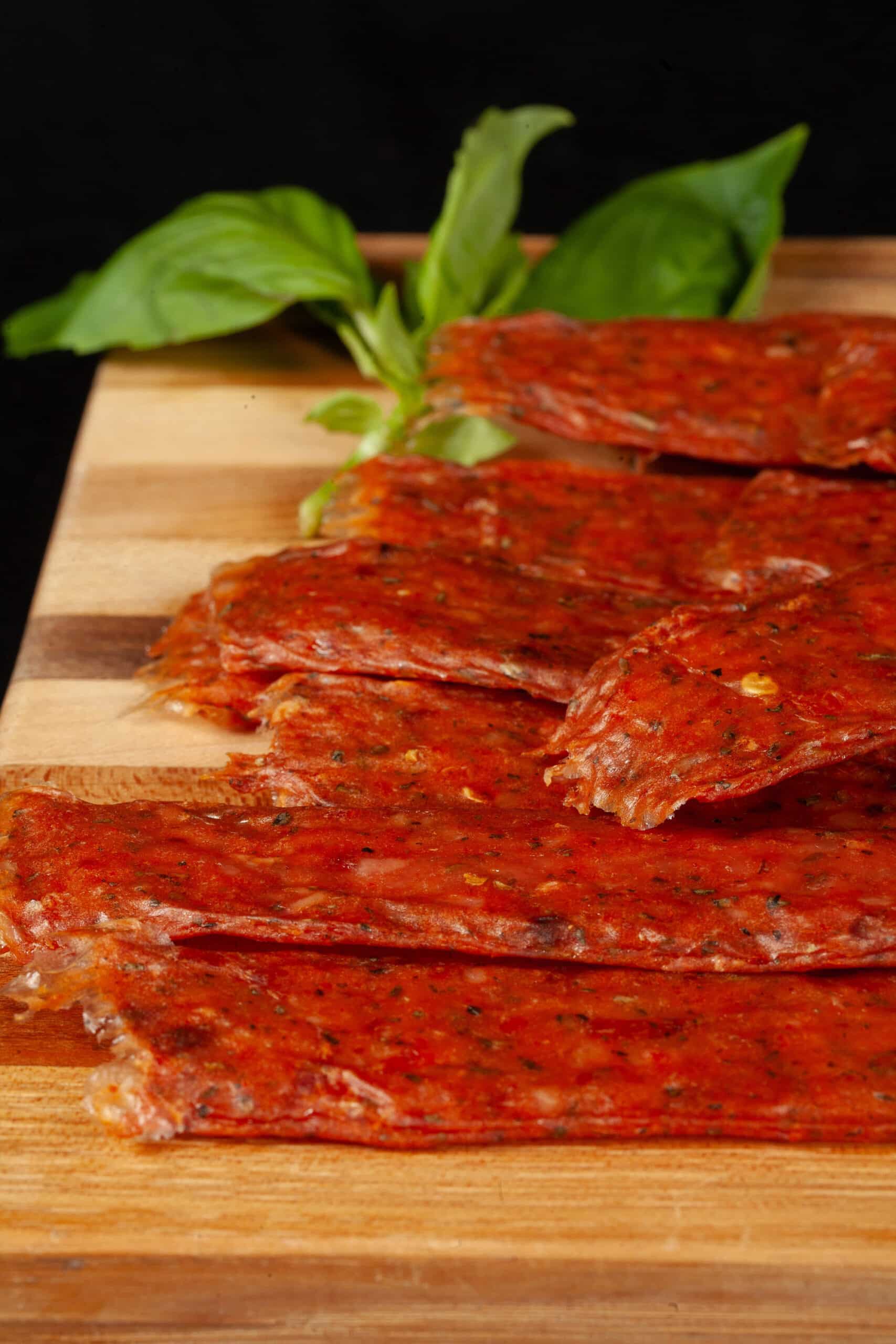 A pile of pizza flavored jerky on a cutting board, with some fresh basil.