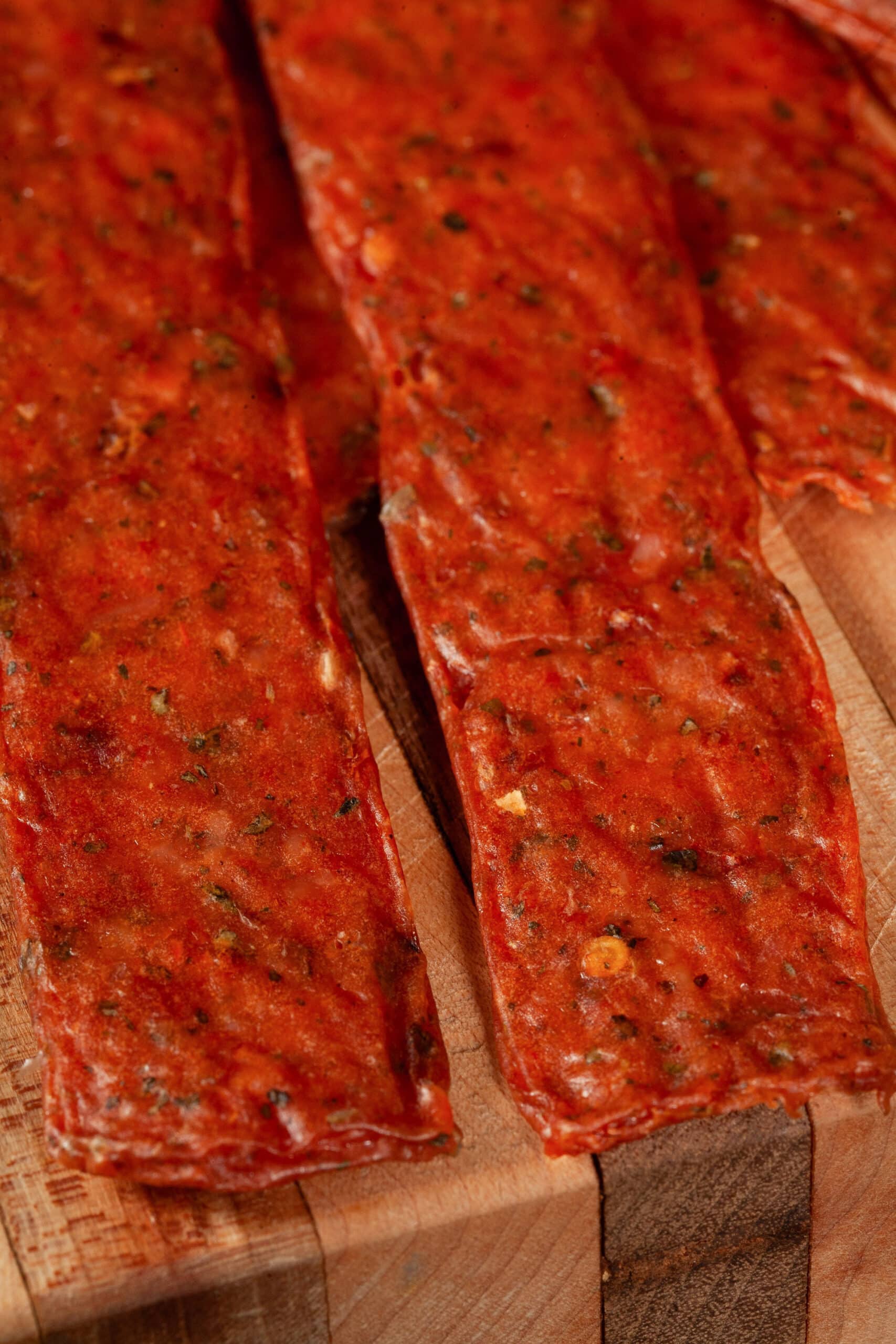 A pile of pizza flavored chicken jerky on a cutting board, with some fresh basil.