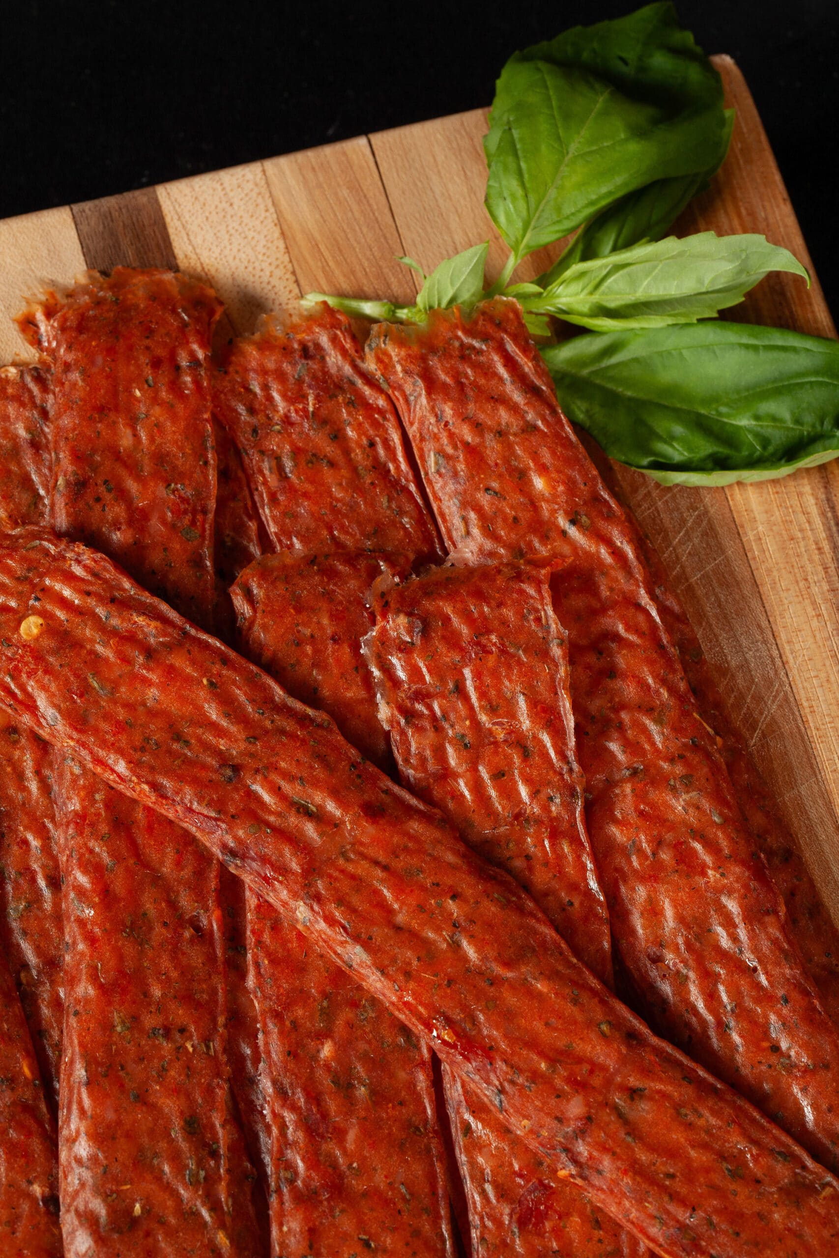 A pile of pizza jerky strips on a cutting board, with some fresh basil.