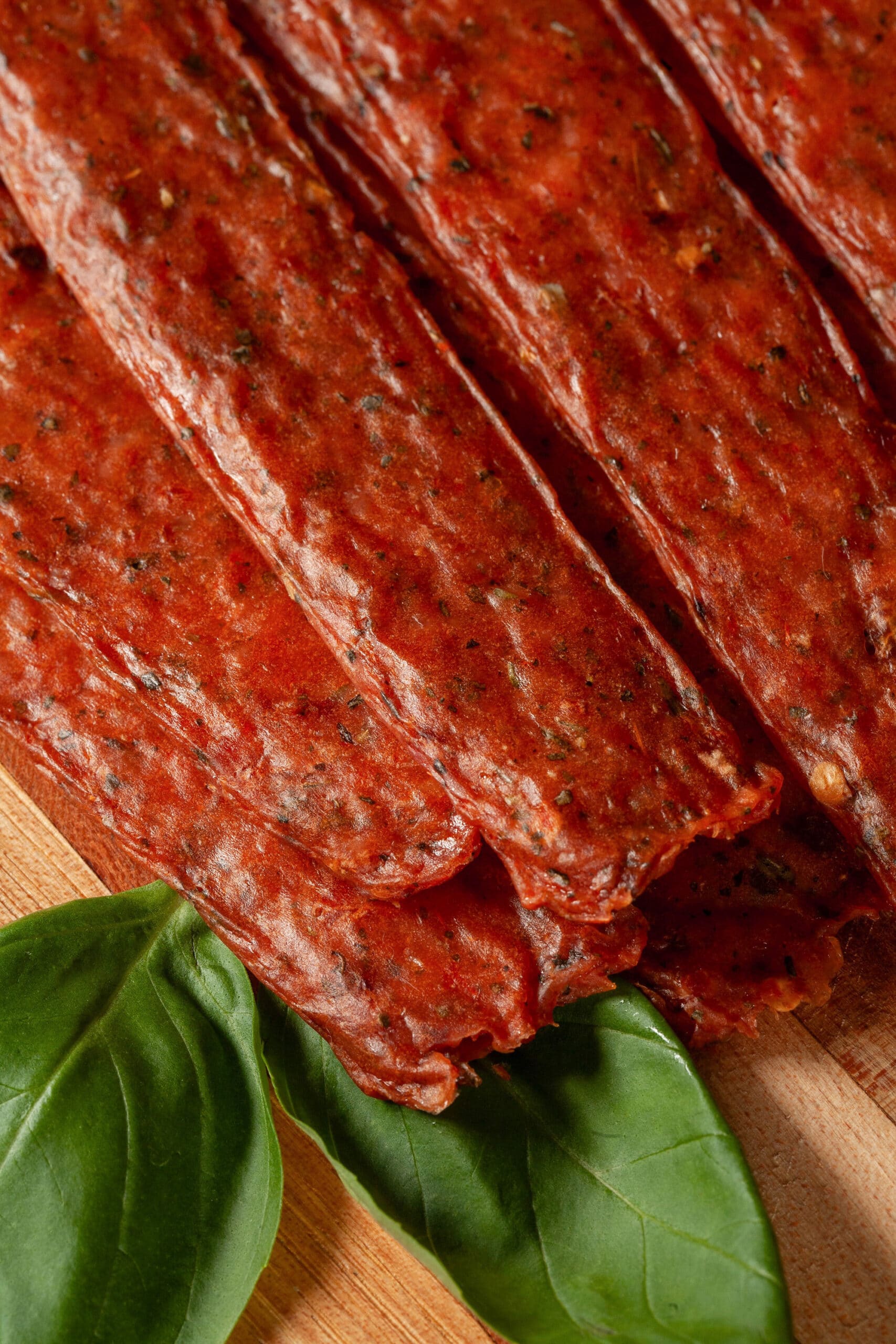 A pile of pizza flavored jerky on a cutting board, with some fresh basil.