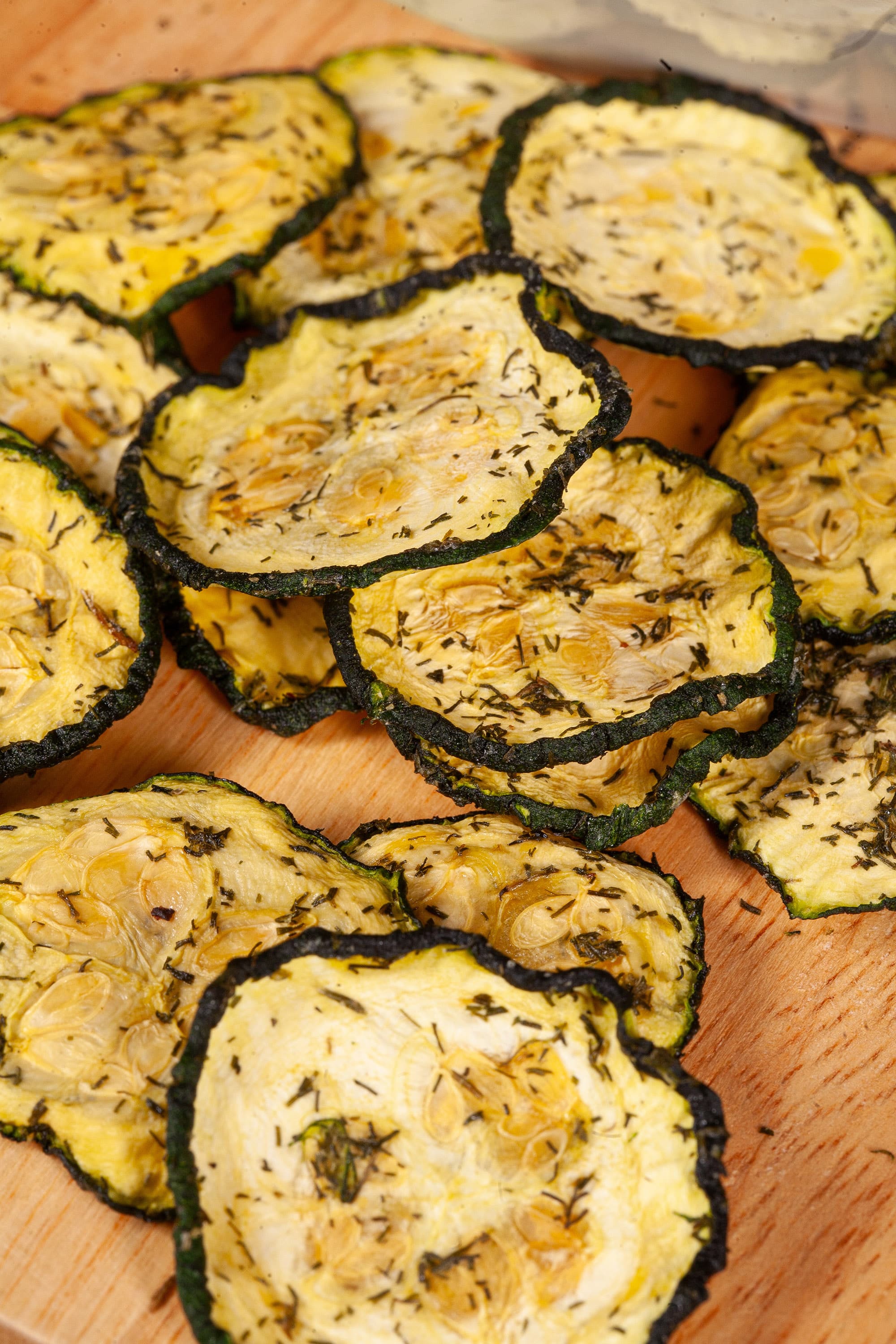 A pile of homemade crunchy dill pickle zucchini chips on a cutting board.