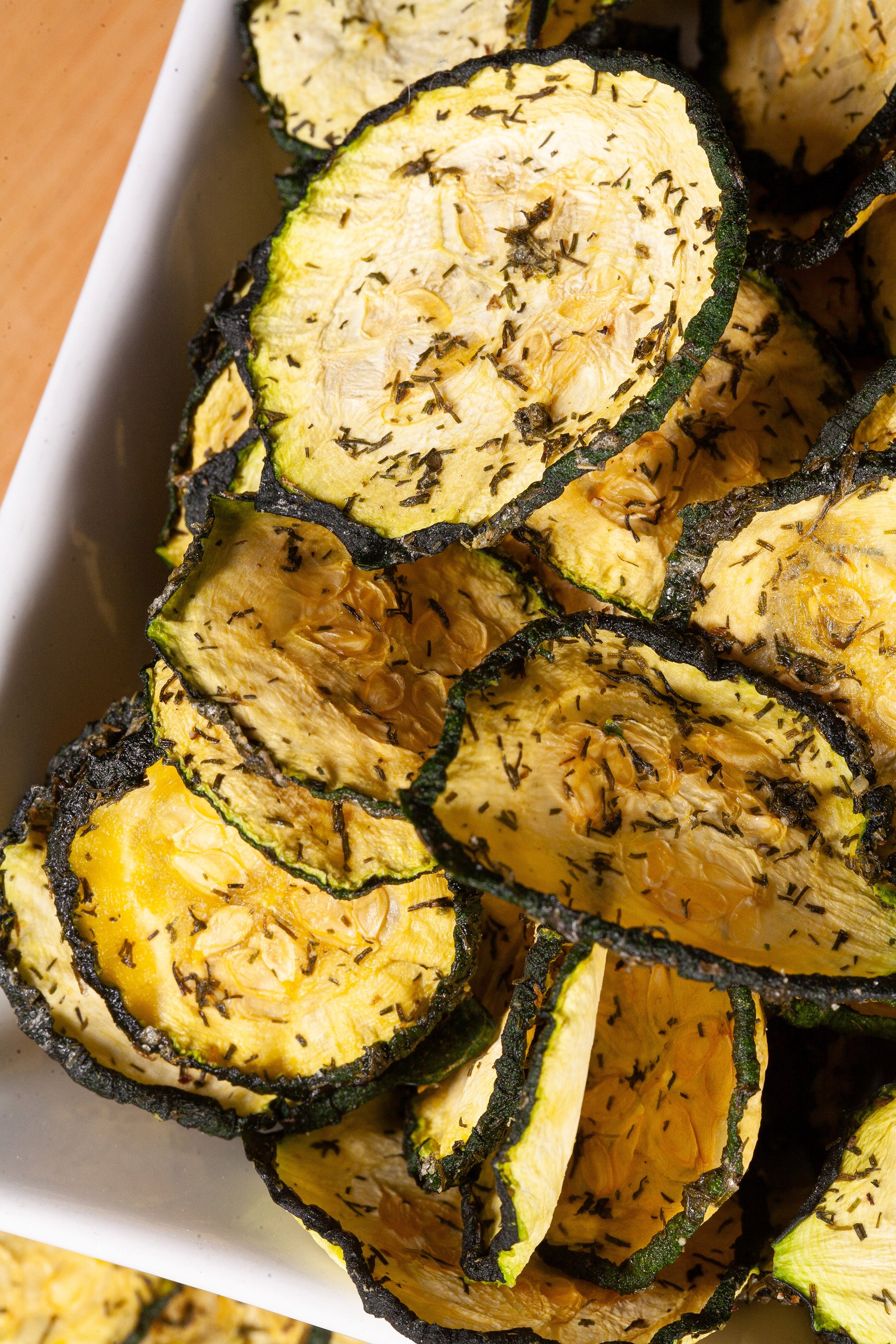 A pile of homemade crunchy dill pickle zucchini chips on a cutting board.