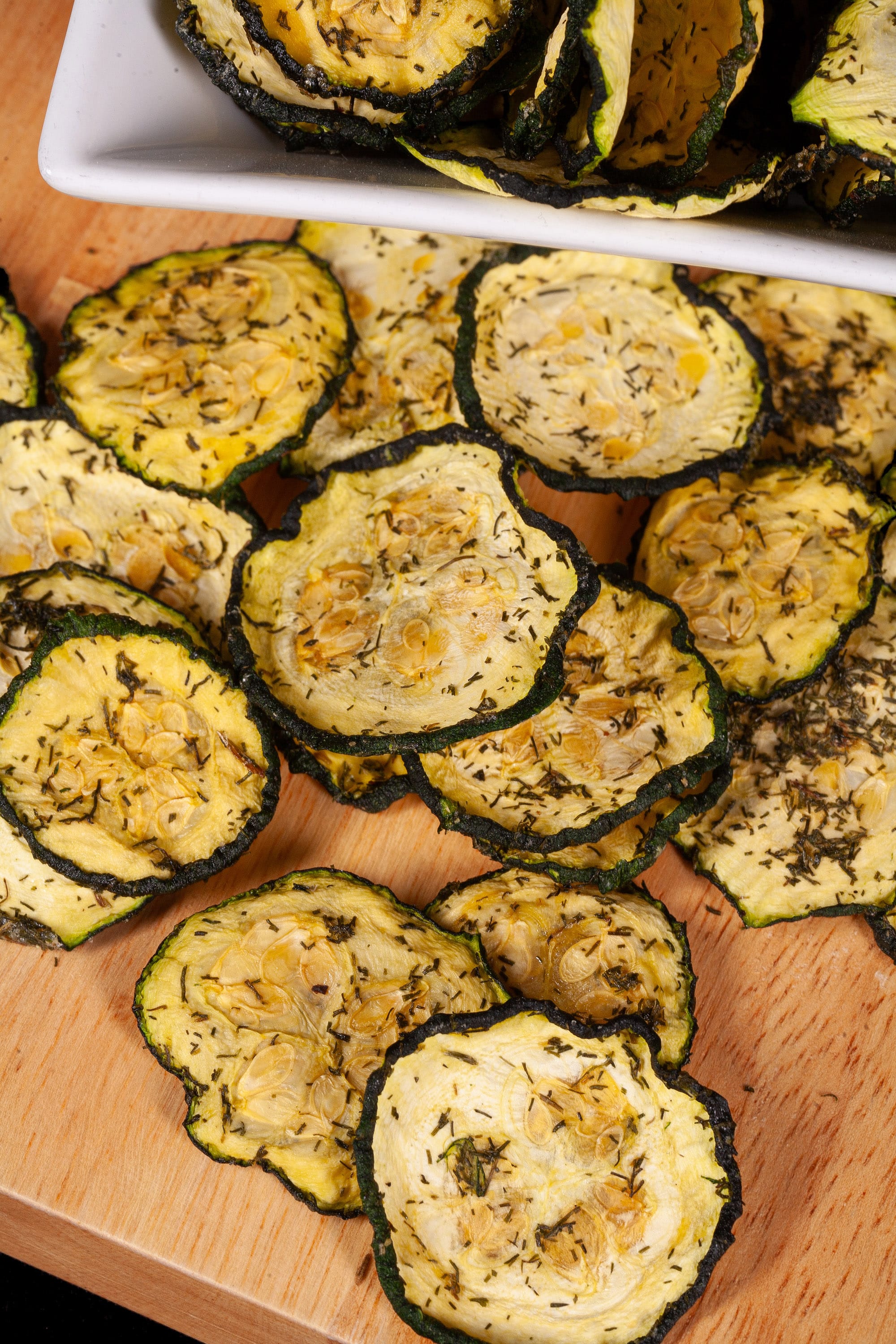 A pile of homemade crunchy dill pickle zucchini chips on a cutting board.