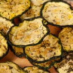 A pile of homemade dill pickle zucchini chips on a cutting board.