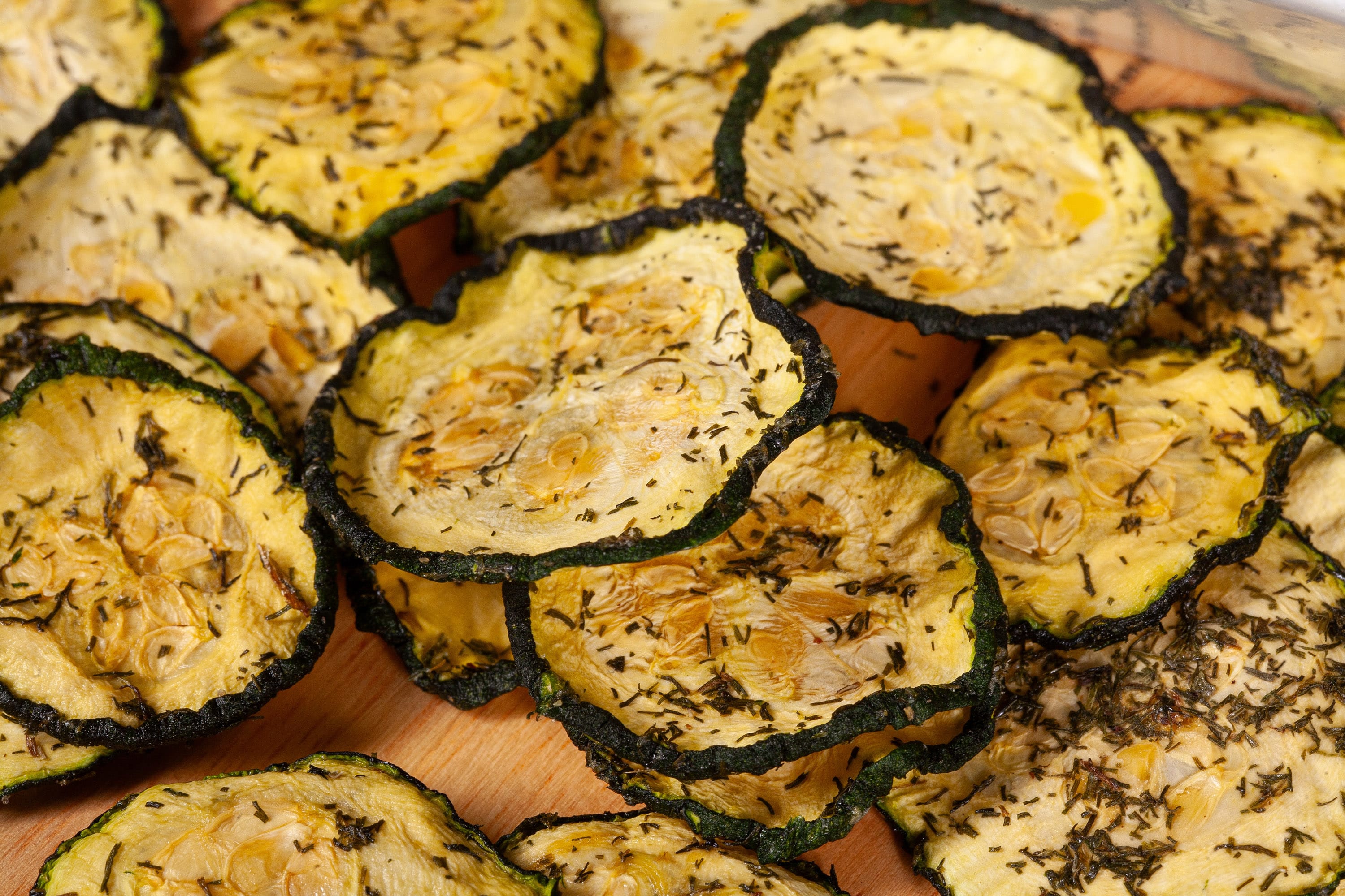 A pile of homemade dill pickle zucchini chips on a cutting board.