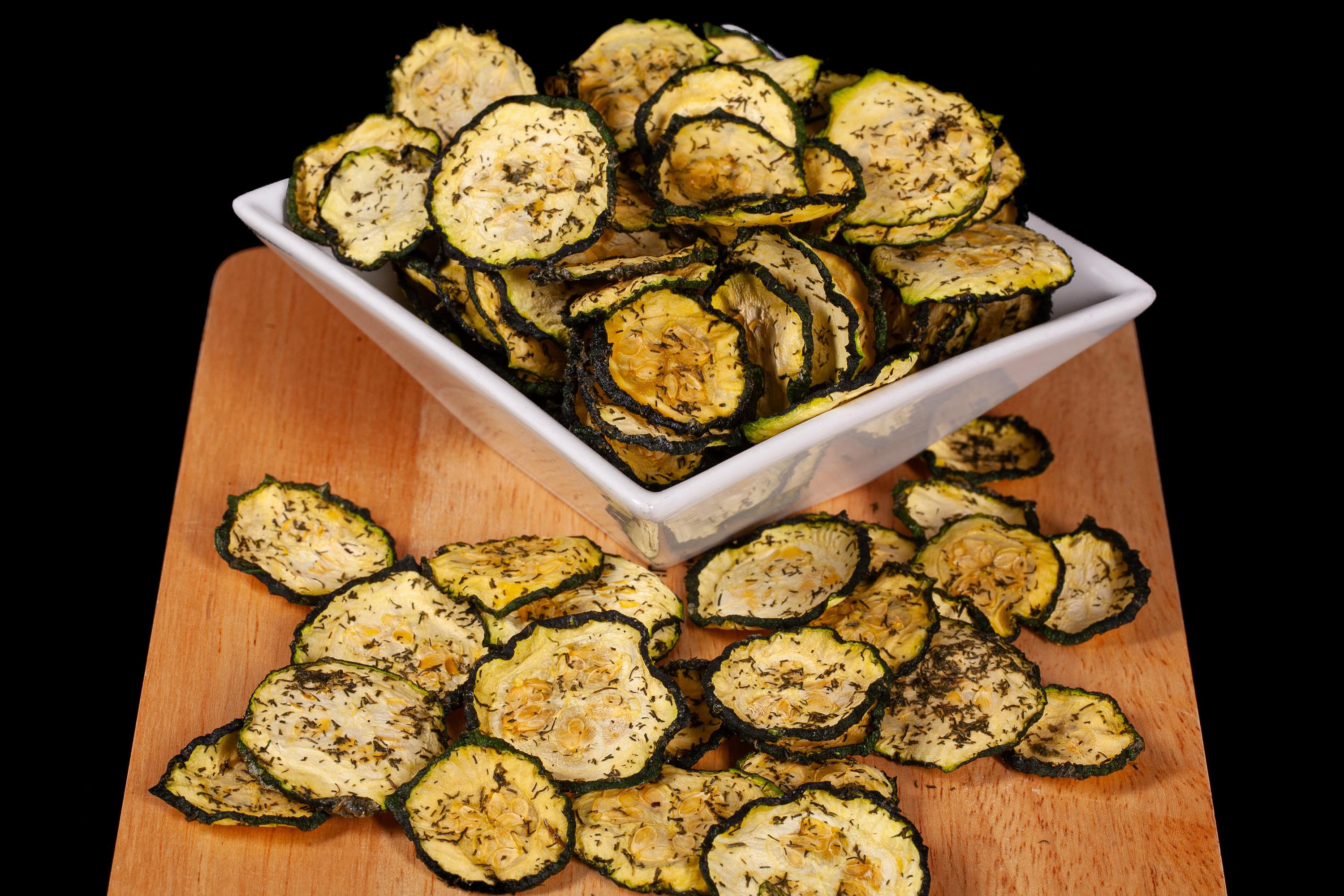 A pile of homemade dill pickle zucchini chips on a cutting board.