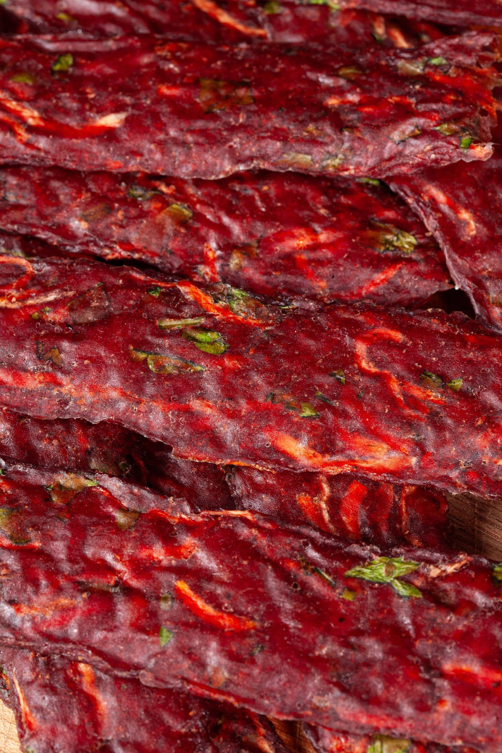 Several strips of Irish Stew beef jerky on a cutting board, with carrots, turnips, and parsley visible in the homemade beef jerky.