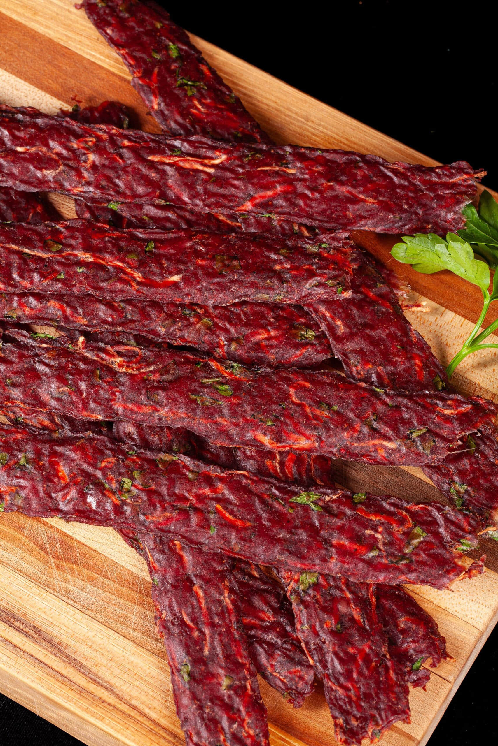 Several strips of Irish Stew beef jerky on a cutting board, with carrots, turnips, and parsley visible in the homemade beef jerky.