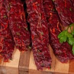 Several strips of Irish Stew beef jerky on a cutting board, with carrots, turnips, and parsley visible in the homemade beef jerky.