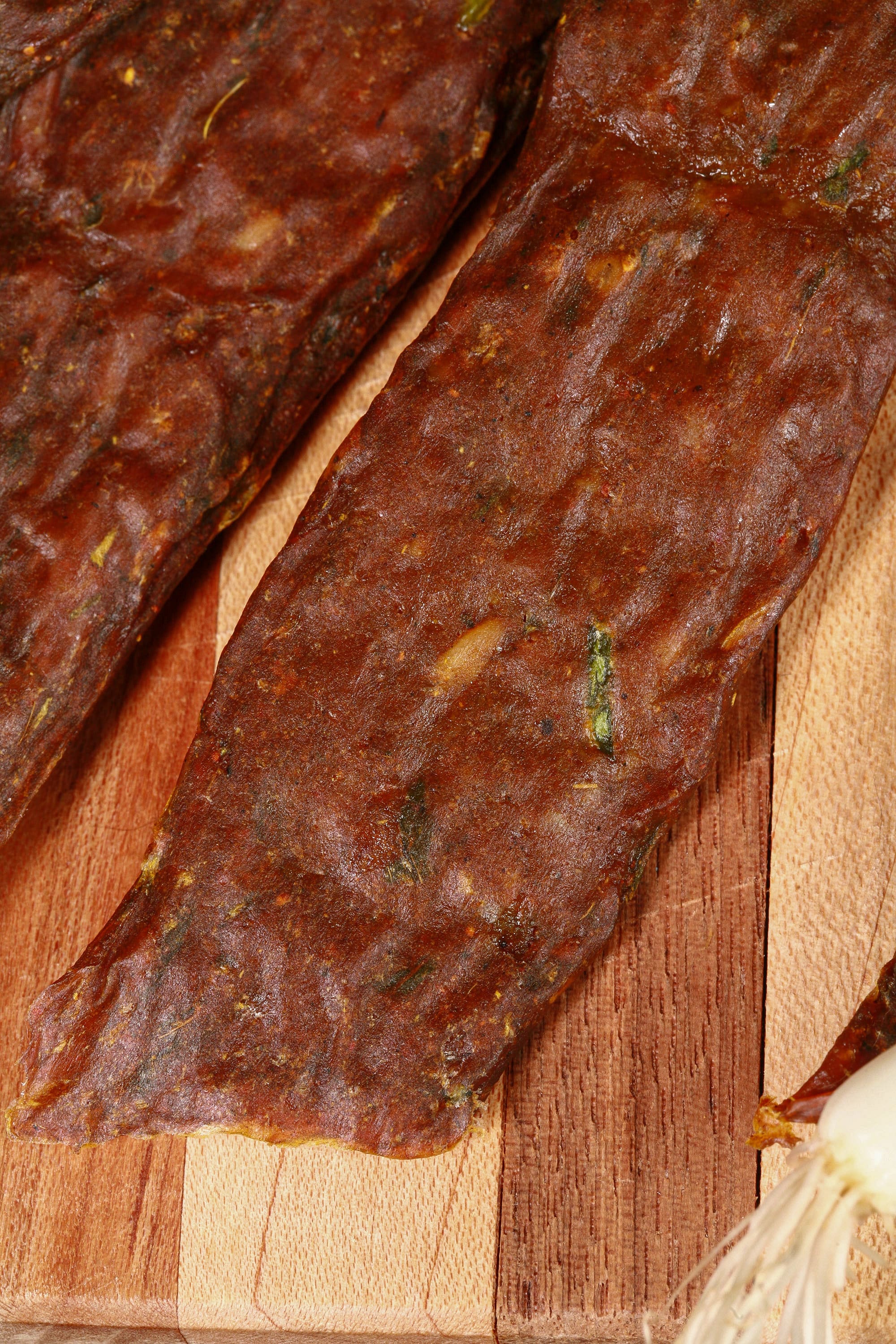 A pile of Trinidadian curry inspired chicken jerky sticks on a cutting board with green onions, garlic, and scotch bonnet peppers.