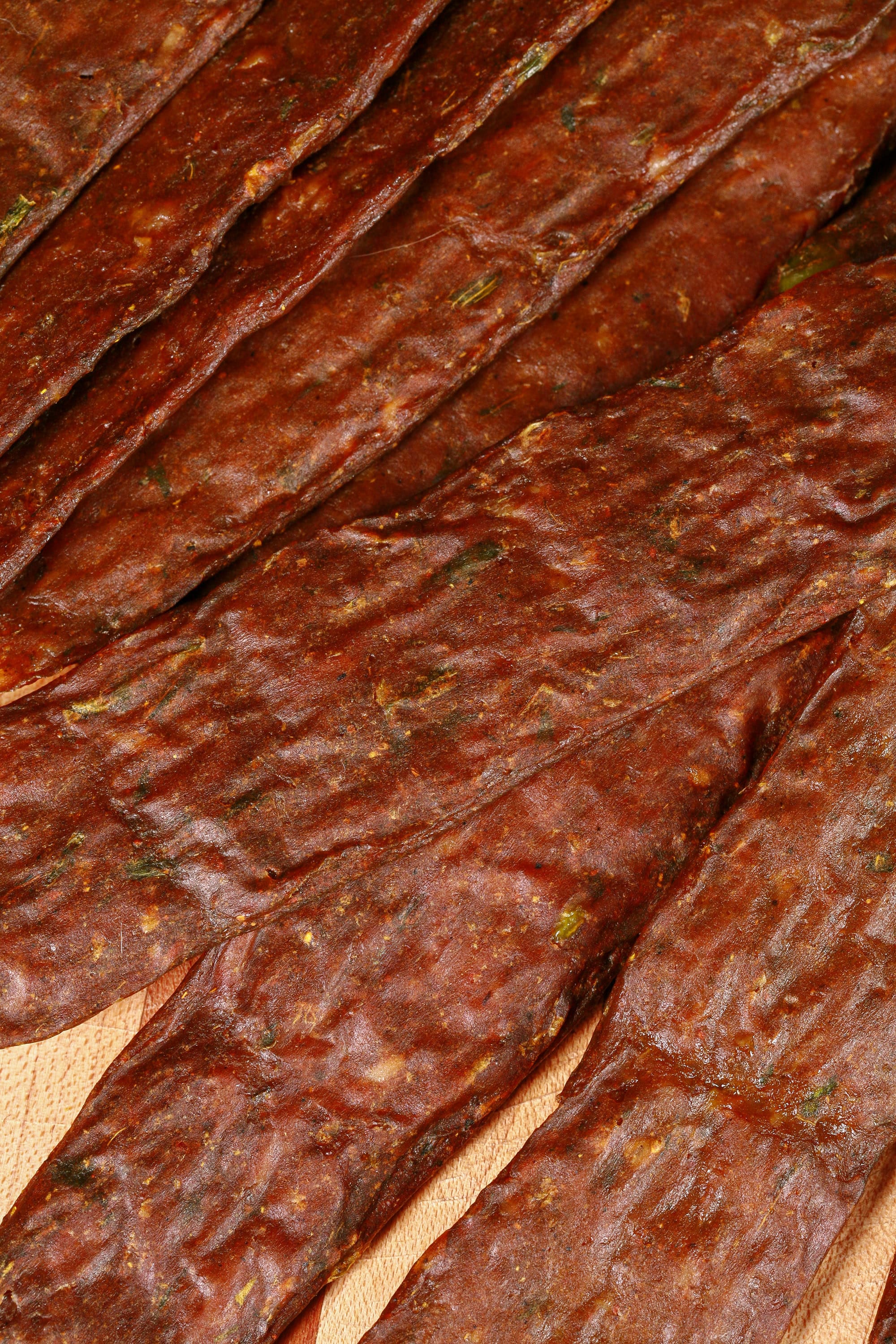 A pile of Trinidadian curry inspired chicken jerky sticks on a cutting board with green onions, garlic, and scotch bonnet peppers.
