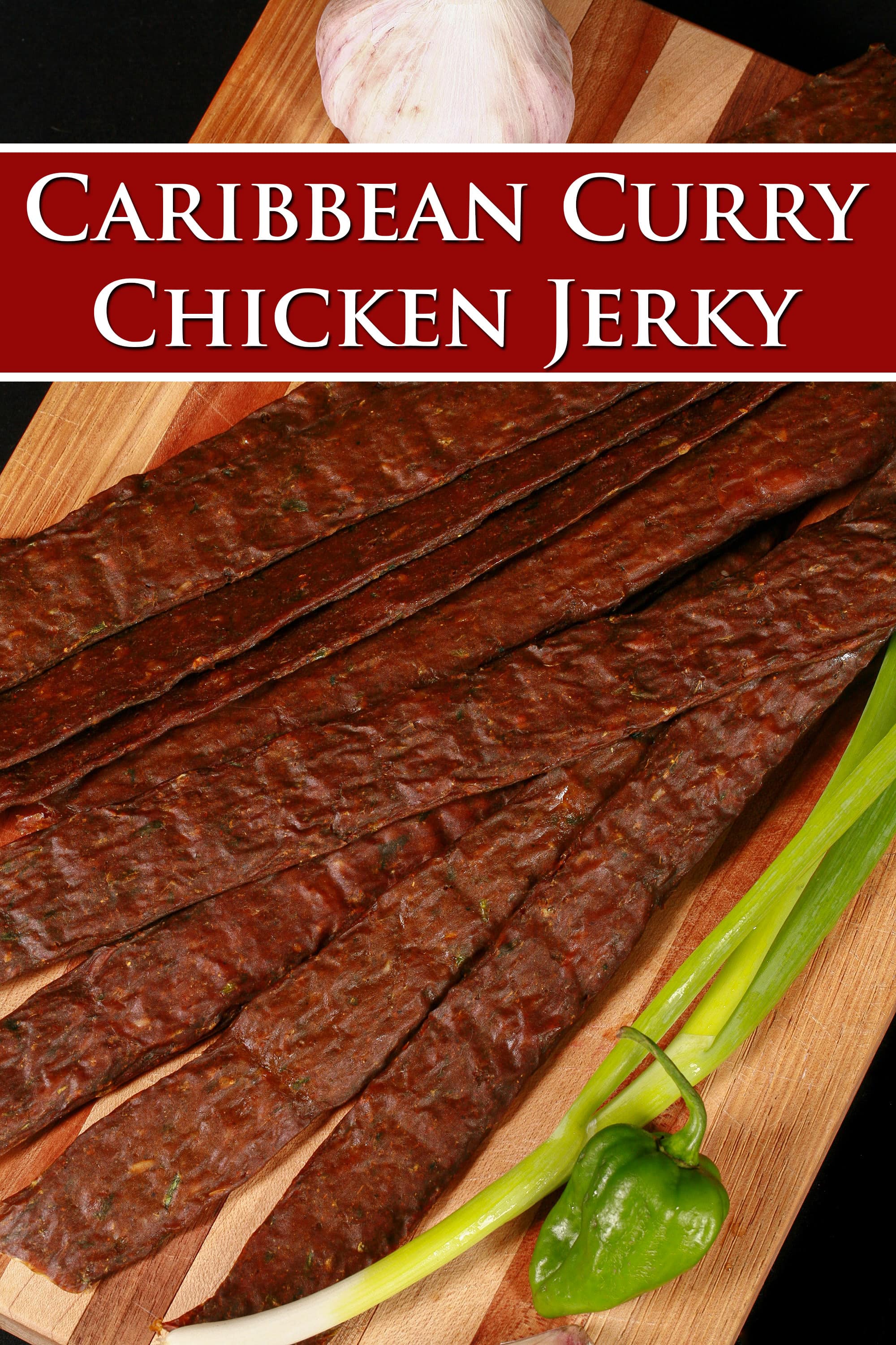 A pile of Trinidadian curry inspired chicken jerky sticks on a cutting board with green onions, garlic, and scotch bonnet peppers. Overlaid text says caribbean curry chicken jerky.
