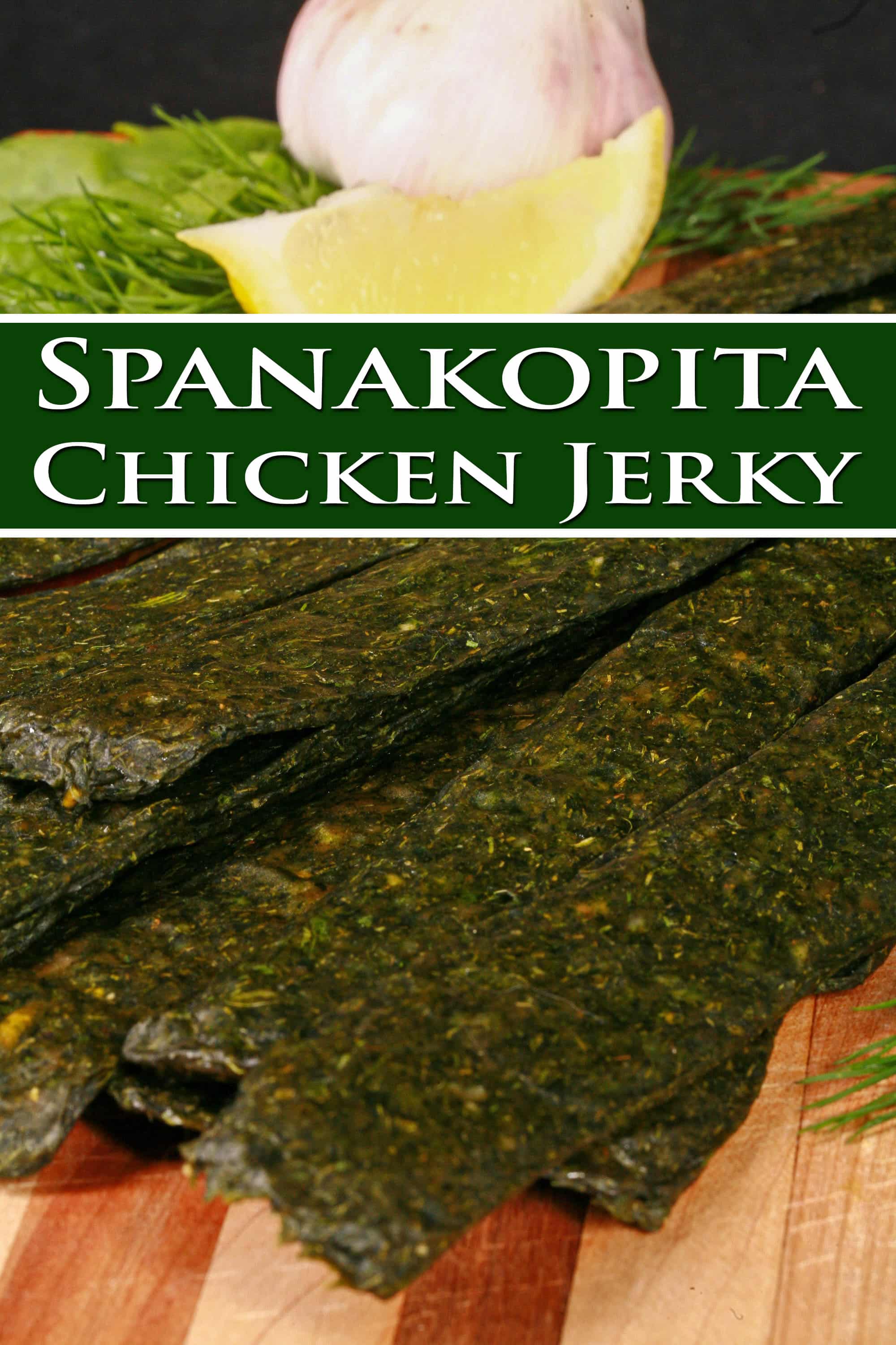 A pile of dark green spinach chicken jerky, with a lemon wedge, garlic, and fresh dill on a cutting board. Overlaid text says spanakopita chicken jerky.